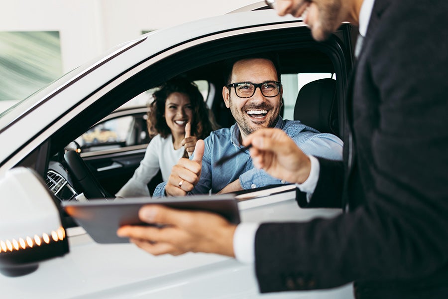 Couple sitting inside white vehicle talking to dealer associate through driver window